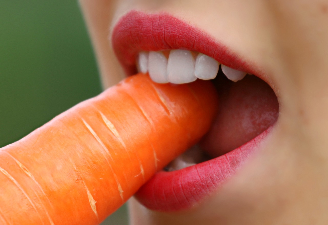 kvinde med pæne tænder tager et bid af en gulerod
